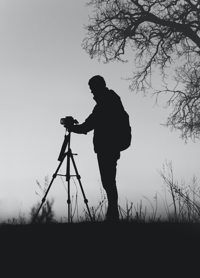 剪影照片的男人面前的单反相机与三脚架无叶的树下

